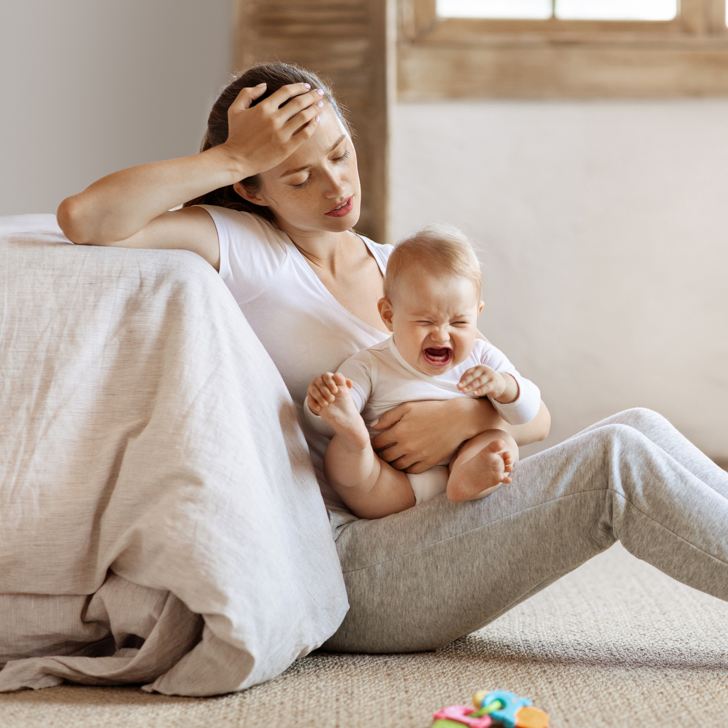 Woman holding a crying baby on a carpeted floor with toys around